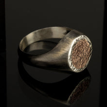 A view of the ring held between fingers to show the scale and the raw metallic contrast.