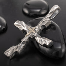 Handmade silver cross pendant model P-178 with a rugged, dark brutalist texture and a small 14K gold cross in the center, displayed on smooth black river stones.